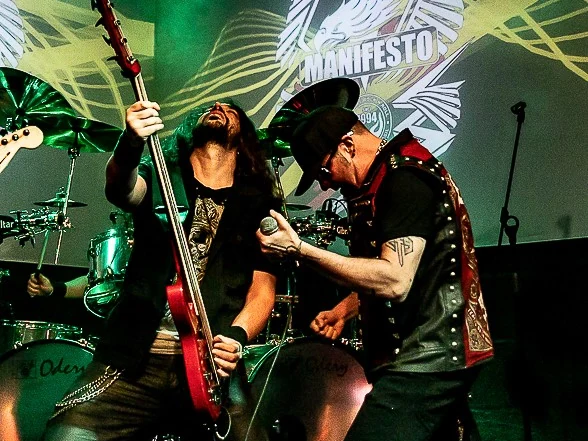 Fabio Carito playing a red bass face to face with Tim "Ripper" Owens, who sings into the microphone